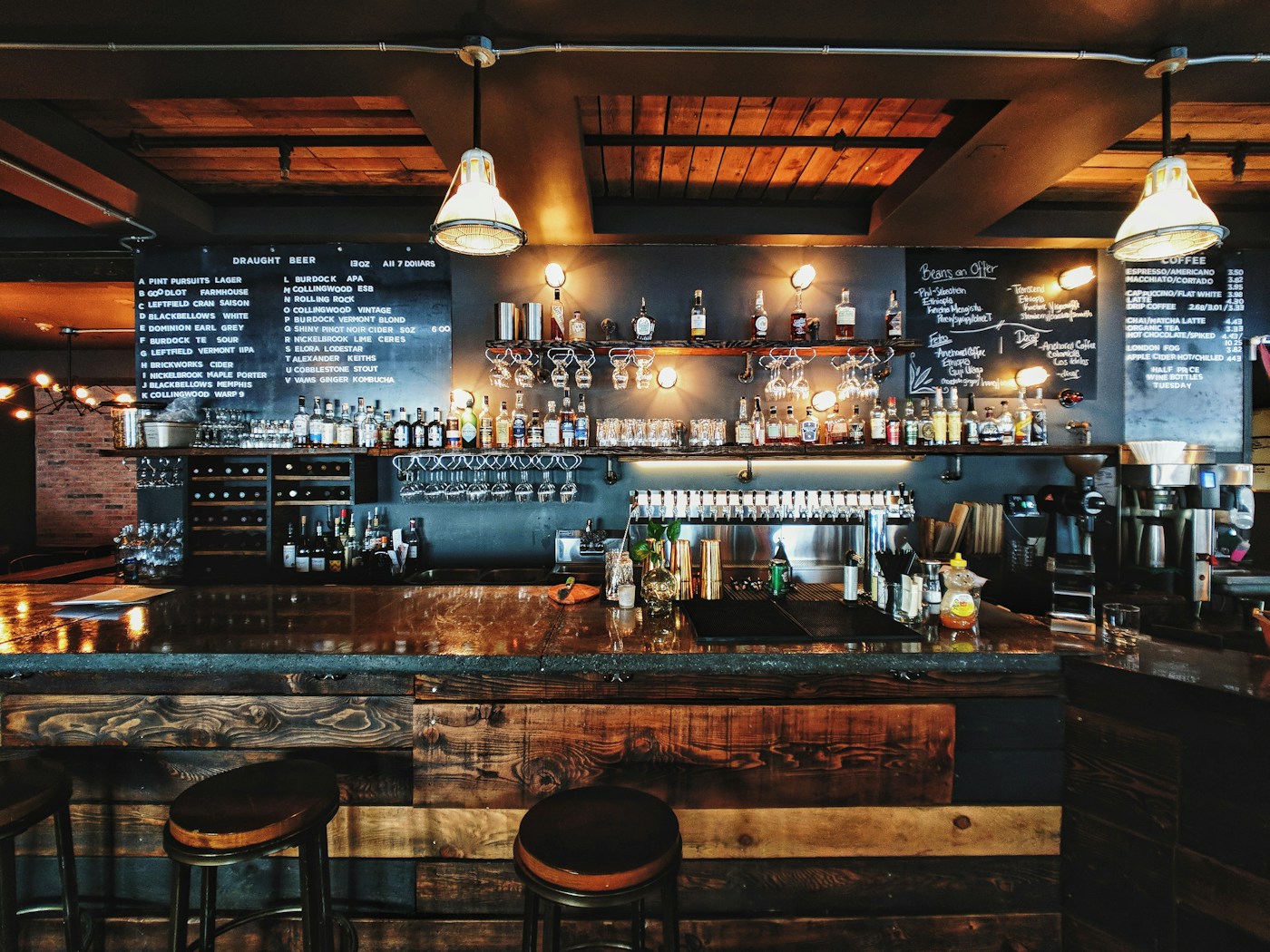 An inviting bar with amber lamps, dark wood and a long counter